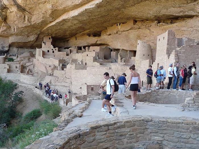 Visitors touring a large, ancient, stone-masonry villageVisiting Cliff Palace on a ranger-guided tour
