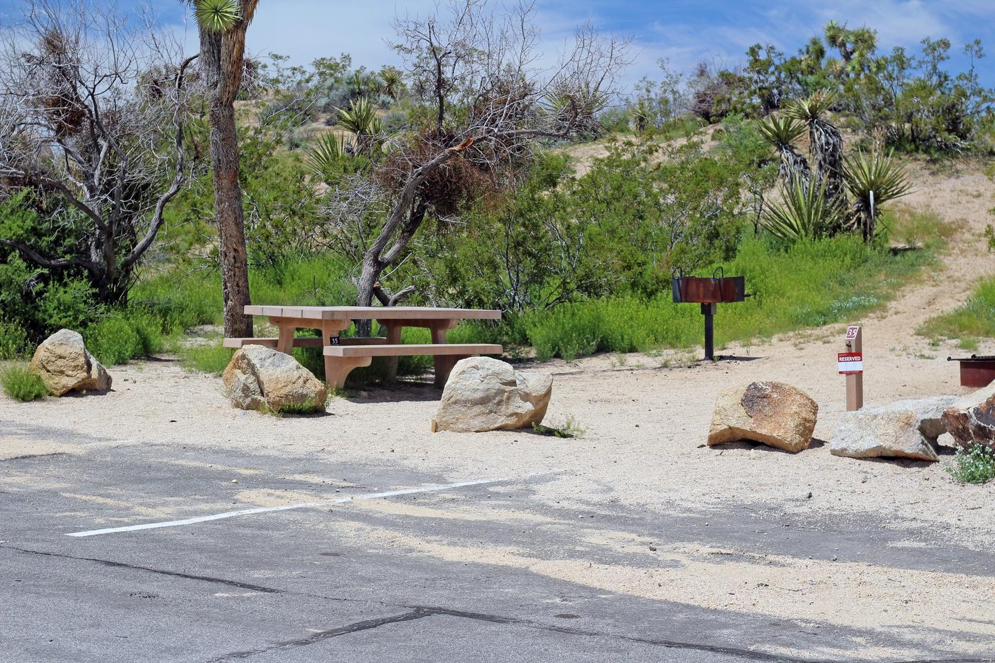 Parking for campsite. Picnic table surrounded by boulders and green plants.Shared parking for campsite.