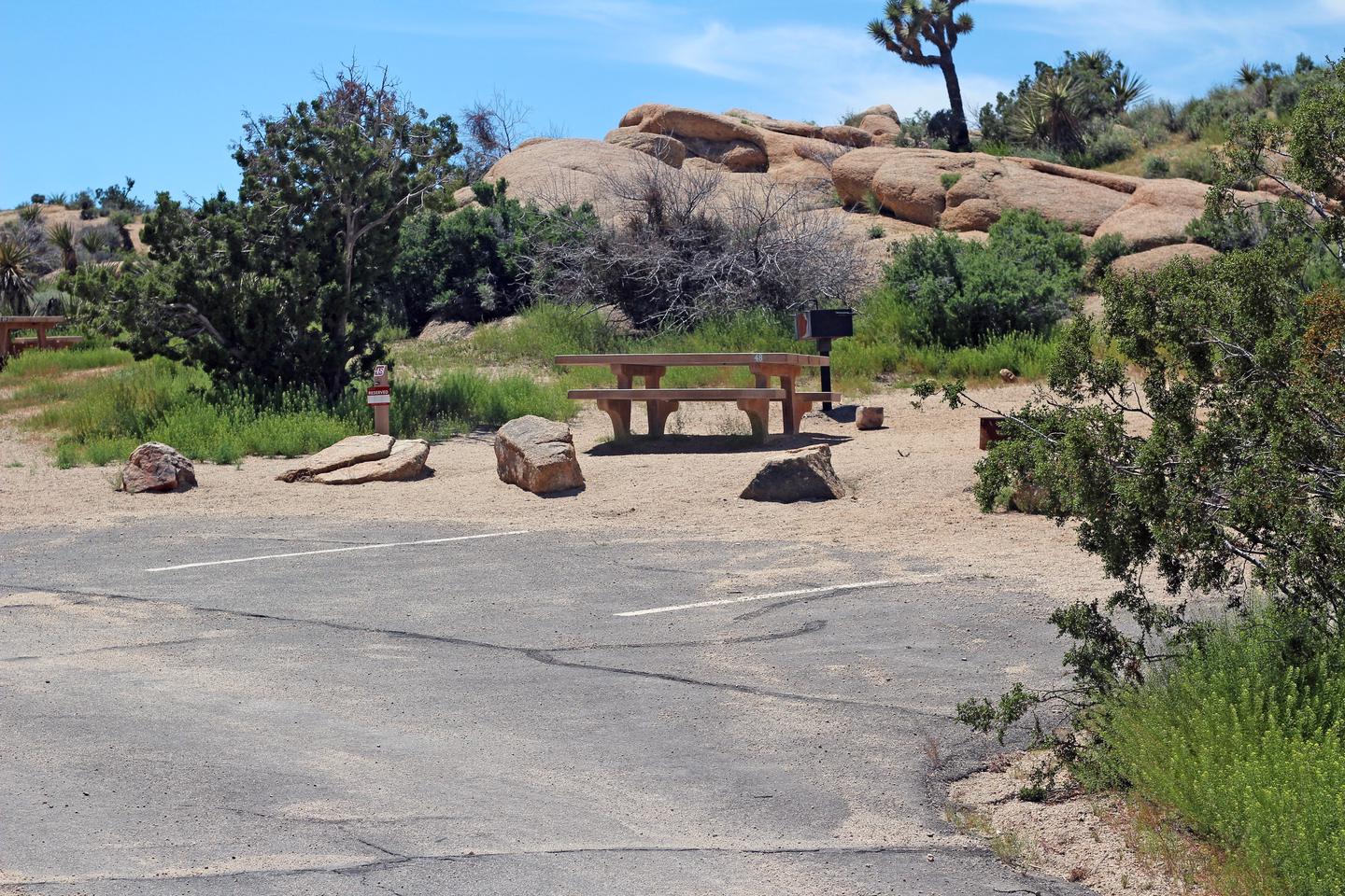 Parking for campsite. Picnic table surrounded by boulders and green plants.Parking and campsite.