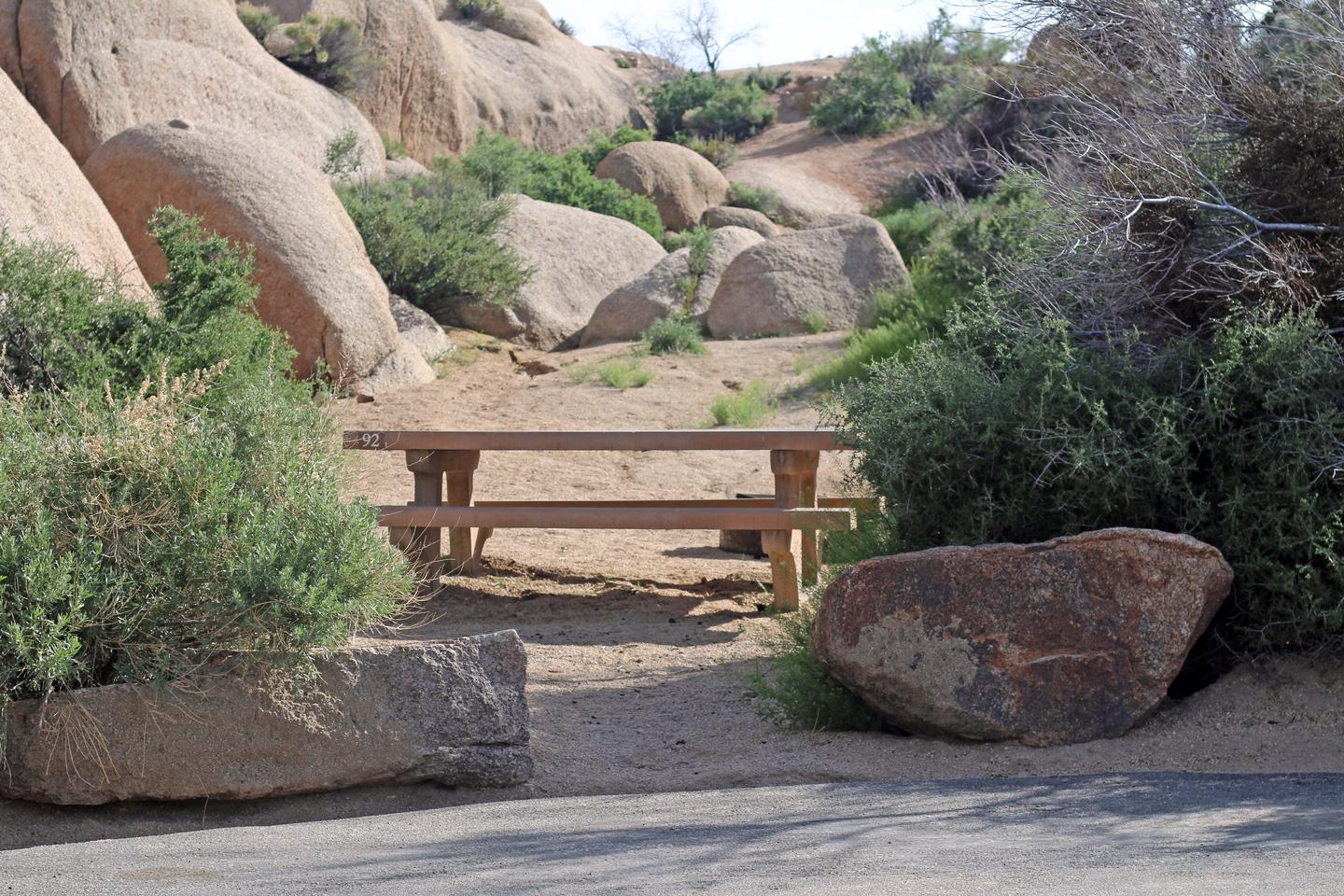 Campsite  with picnic table surrounded by boulders and green plants.Campsite.