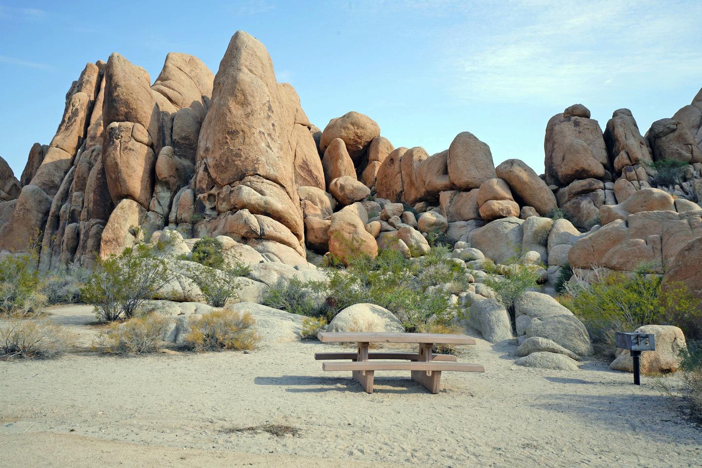 Picnic table surrounded by boulders and green plants.Campsite.