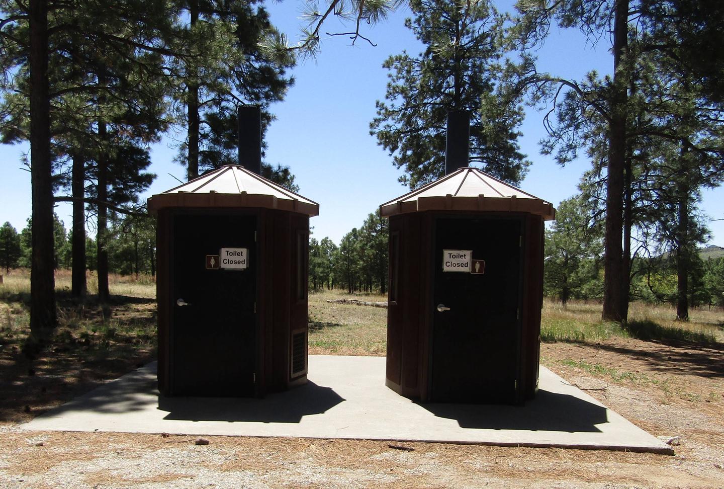 Two vault toilets with pine trees behindVault toilets are present at Ponderosa Group Campground. No running water is available in restrooms. No shower facilities in the park.