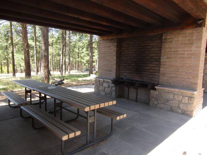 Two picnic tables under a covered shelter with grills built into the wallInside of Campsite B's covered cooking shelter