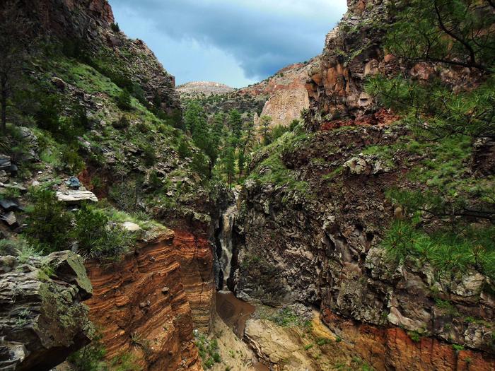 A water fall flows between plant covered rock facesBandelier contains over 70 miles of hiking trails, including the Falls Trail,  that explore the varied landscapes and ecosystems of the Pajarito Plateau.