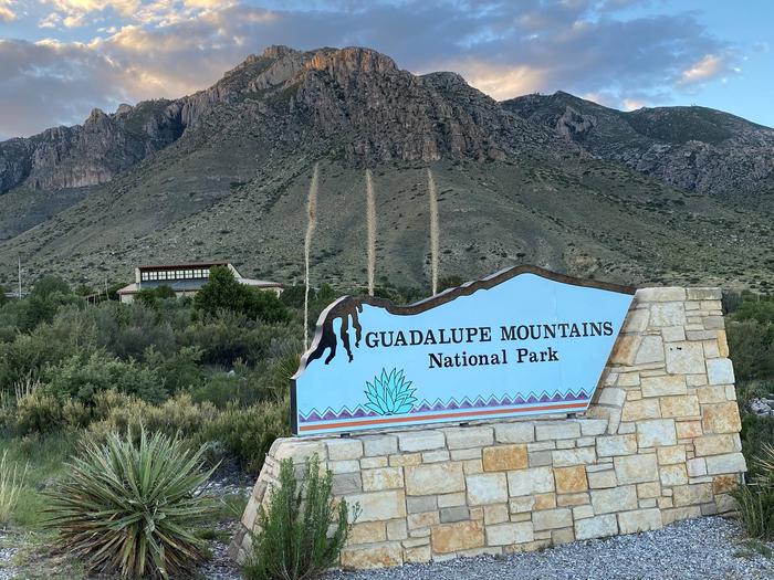 Guadalupe Mountains National Park entrance sign underneath sunkissed Hunter Peak with visitor center in midground.Pine Springs Entrance Sign & Visitor Center at Guadalupe Mountains National Park, 