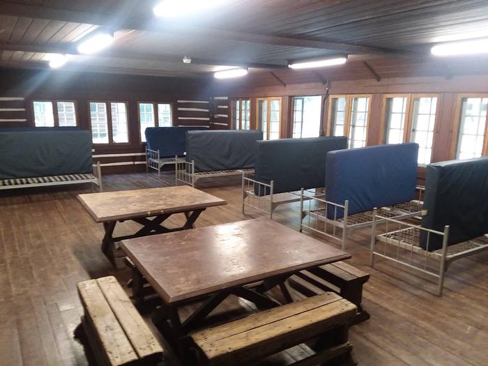 Interior of lodge. 2 square tables and 4 benches.  8 single metal cots with vinyl covered mattresses.Interior of a Camp Misty Mount lodge. 2 square tables and 4 benches.  8 single metal cots with vinyl covered mattresses.  
