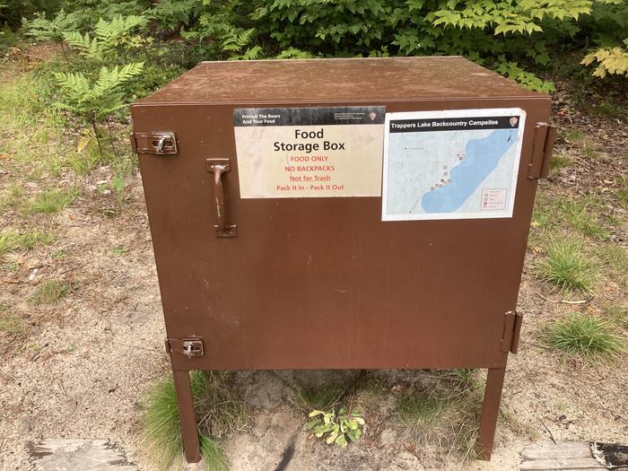 A bear proof container in the woods with a map on it.