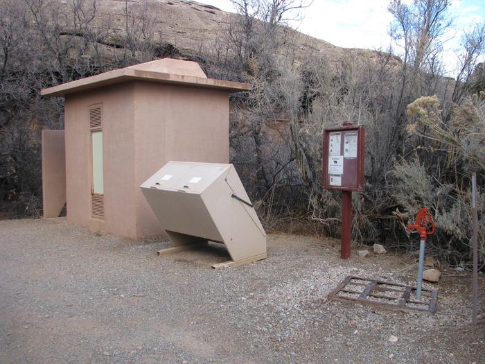 Vault toilet, trash can, and potable water spigot alongside the driveway leading to the split top group site. 