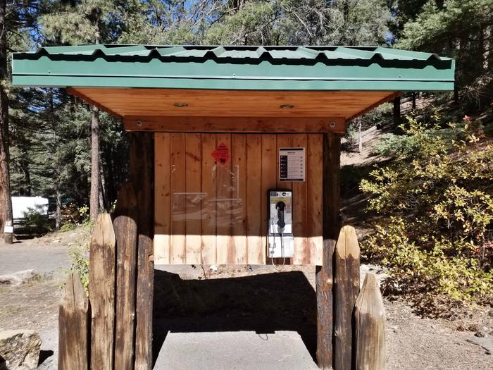 A payphone located underneath a  wooden kiosk with a green metal roof.Campground payphone