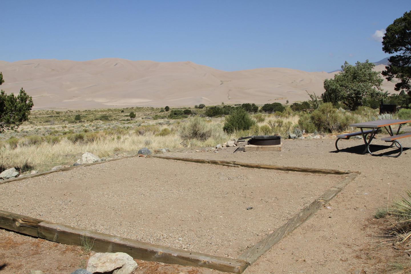 Back view of Site #39 designated tent pad, fire ring, and picnic table. Great Sand Dunes in the background.Site #39, Pinon Flats Campground
