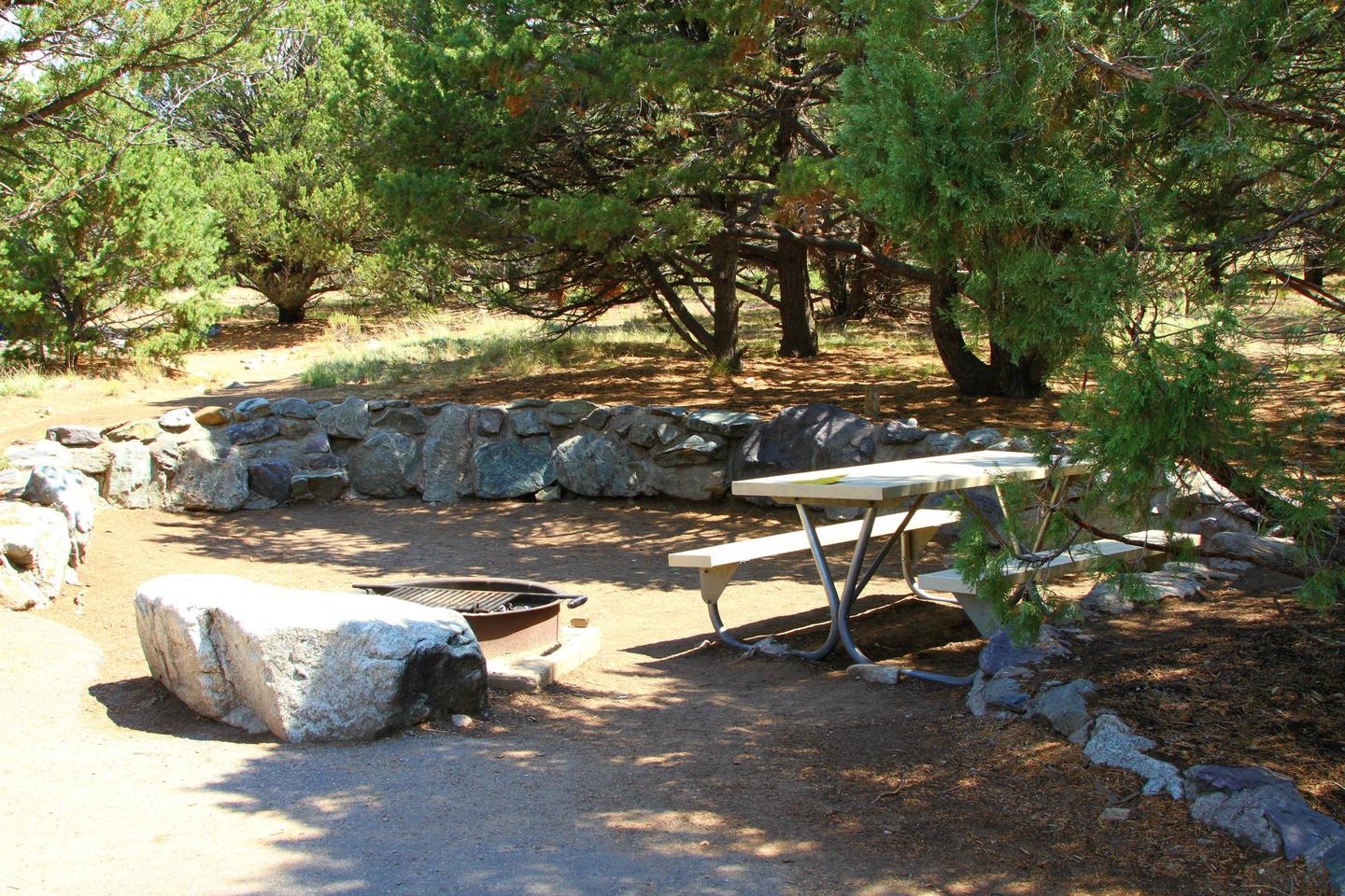 Side view of Site #51 tent pad, with fire ring and picnic table. Tent pad area is marked with a short rock wall on three sides.Site #51, Pinon Flats Campground