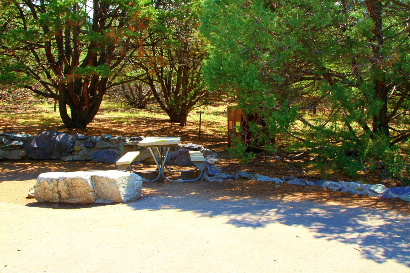 Closer view of Site #51 tent site, picnic table, and bear box. Medium boulder acts as a boundary between the parking pad and the tent area. Site #51, Pinon Flats Campground