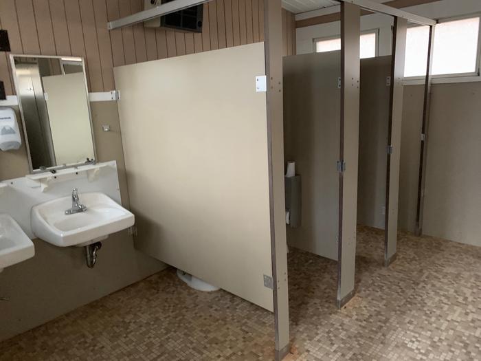 Partial interior view of comfort station.  2 small bathroom stalls, 2 windows, 2 porcelain sinks with mirrors.  Flooring is tile,Each of the two comfort stations are divided and have separate facilities for women and men. Both  have toilets, sinks, mirrors and hand dryers. They are cleaned and stocked daily with hand soap and toilet paper. 