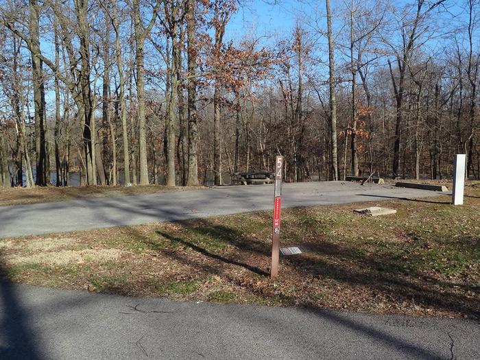 This site is nestled in the trees providing shade. The picnic table and fire pit are to the left of the concrete pad. The picnic table sits on a paved pad. This is a full hookup site and all hookups are located on the right. 