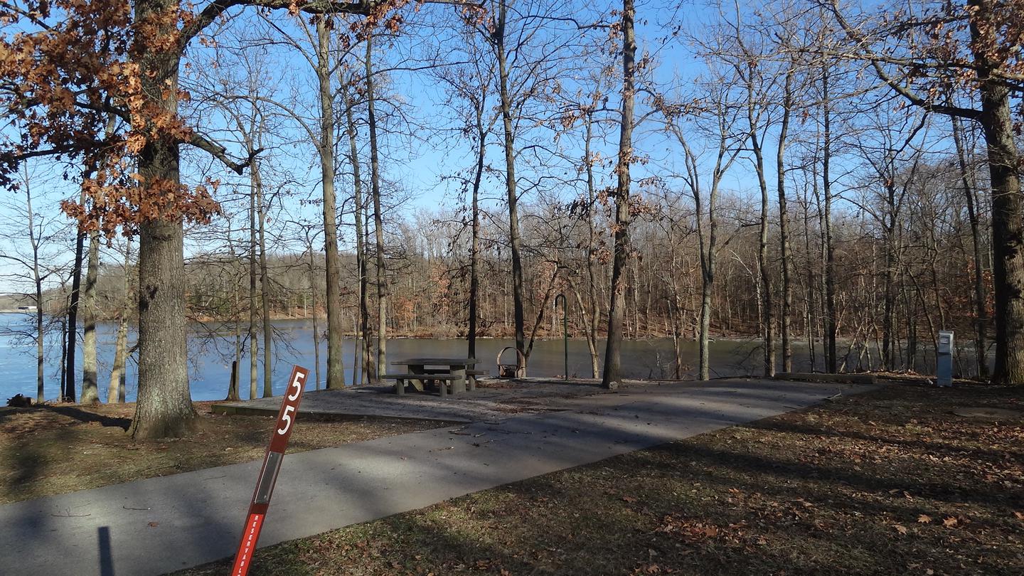 This site is located near the water, providing a great view. There are plenty of trees to provide shade. The picnic table and fire pit are on the left side of the site and electric hookup is located to the right. 