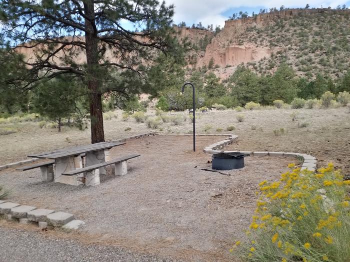 A campsite with a stone picnic table, lantern post, fire ring and a sandstone mesa in the background.