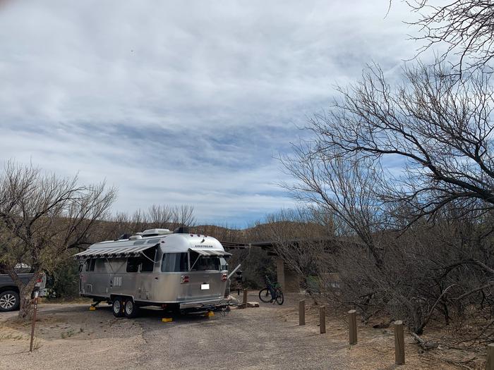A silver trailer in Site 10 is parked in front of the shade shelter. Retractable awnings are all extended out from the trailer. A bicycle sits inbetween the trailer and the shade shelter, waiting to be ridden.Parked trailer in Site 10