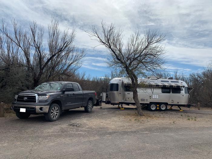 A truck and a silver trailer are parked in the pull-through space in Site 10. The pull-through is a tight arc and has medium-sized trees growing on either side of it.Parked truck and trailer in Site 10