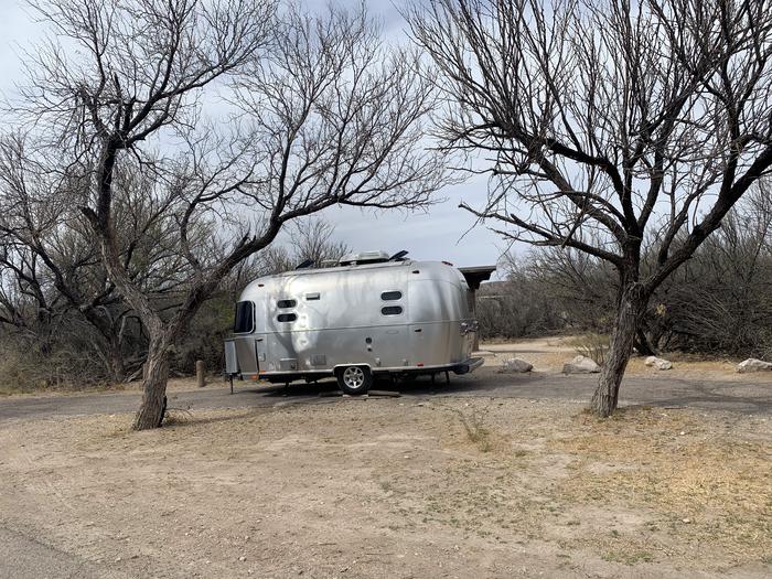 View of a medium-sized trailer parked in the long, curved driveway. Some trees and low bushes grow intermittently around the site, but all have lost their leaves in winter and offer no shade. . View of a trailer parked in the driveway.