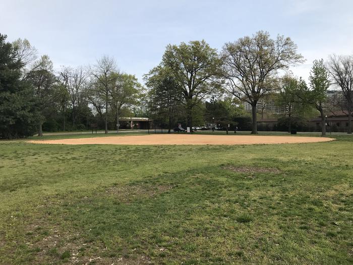 The photo shows field S9 from the outfield. There is a backstop, infield, and grassy area. There are scattered trees in the background.Field S9