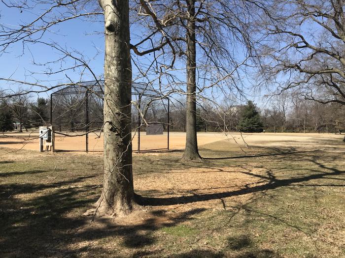 The photo shows field S10 with trees behind a backstop, infield, and grassy outfield. There are scattered trees in the background.Field S10