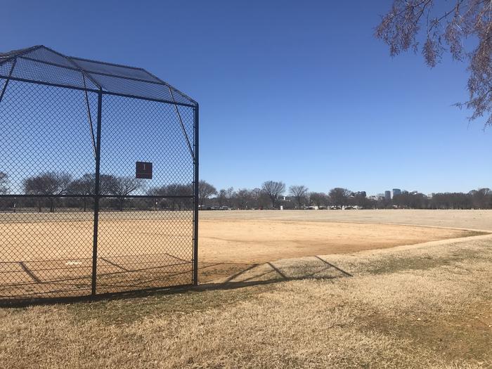 The photo shows a softball field with a backstop, infield, and grassy outfield. There are scattered trees in the background.Field S1
