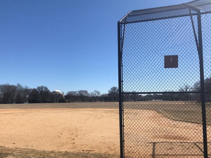 The photo shows a softball field with a backstop, infield, and grassy outfield. The Thomas Jefferson Memorial and scattered trees are visible in the background.Field S4