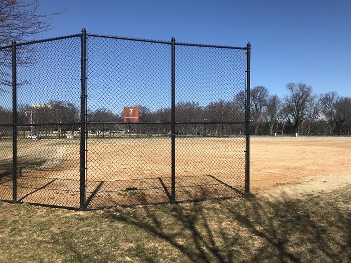 The photo shows a softball field with a backstop, infield, and grassy outfield. The Lincoln Memorial and scattered trees are visible in the background.