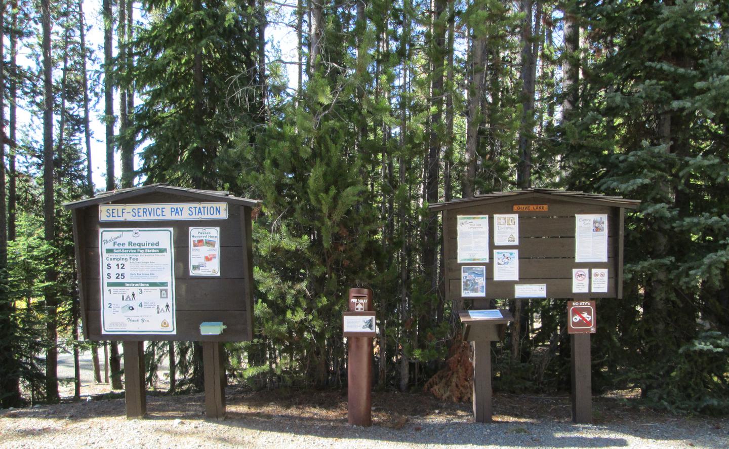 2 information boards with a metal fee vault between and conifers in the backgroundOlive Lake Campground Information and fees