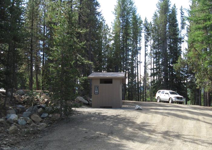 brown vault toilet beside gravel road with white SUV next to pine treesOlive Lake's newest toilet, located near dam.