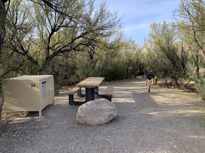 Close-up view of the bear box, picnic table, and metal grill for site 39. A large rock blocks the end of the driveway in front of the picnic table. Close-up view of Site 39