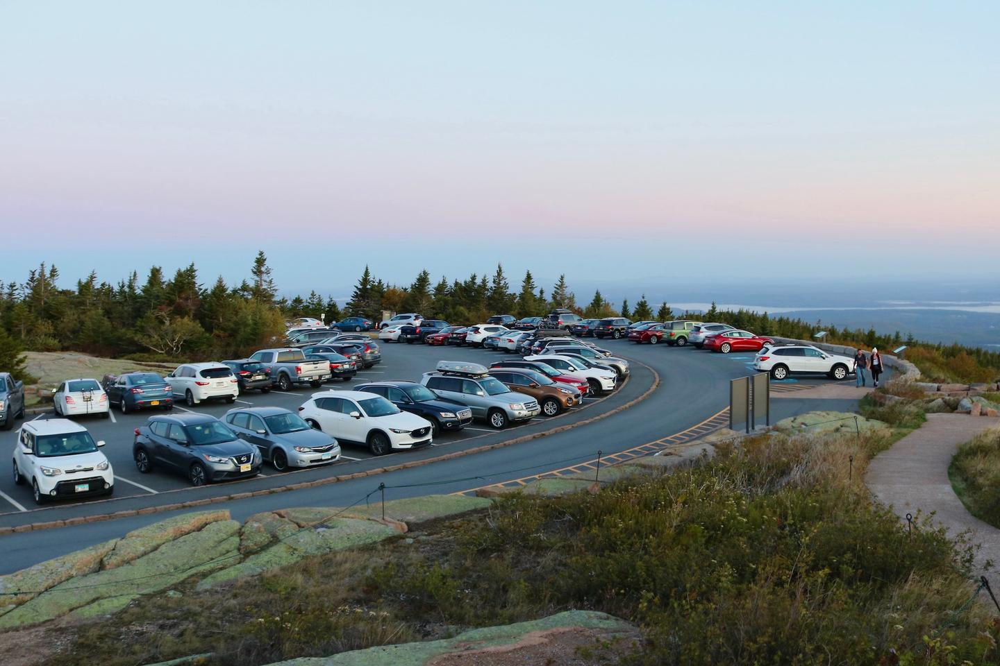 A full parking area on the top of Cadillac Mountain in low light at sunrise surrounded by trees and granite ledges.Parking for sunrise at the Cadillac Summit.