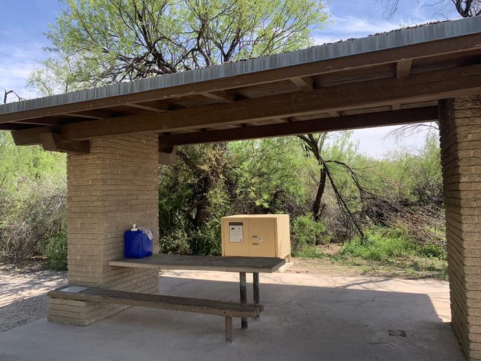 Close-up view of the shade shelter for site 20. There is a picnic table attached to the inside of the shelter and a bear box adjacent to the shelter. Close-up view of the shade shelter for Site 20 