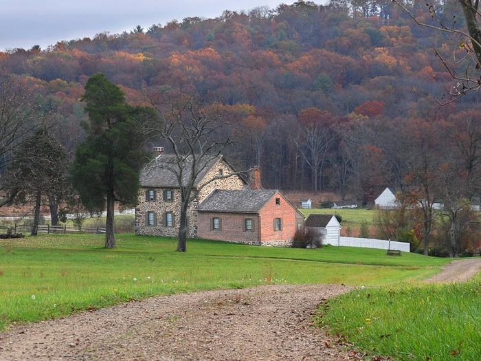 Approach to brick farmhouse with autumn foliage in backgroundThe Historic Bushman House