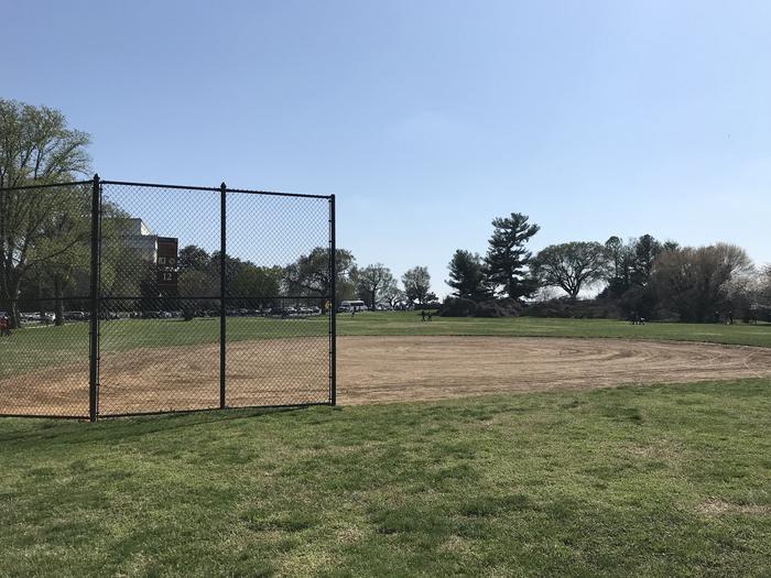 The image shows field S12 with a backstop and infield in the foreground, and a grassy outfield, scattered trees, and the Lincoln Memorial visible in the background.Field S12