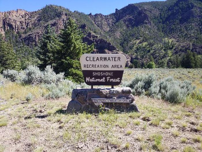 Yellow and brown campsite sign mounted on a rock pedestal. Trees, mountains and a little bit of blue sky are in the background.Clearwater Campground Sign