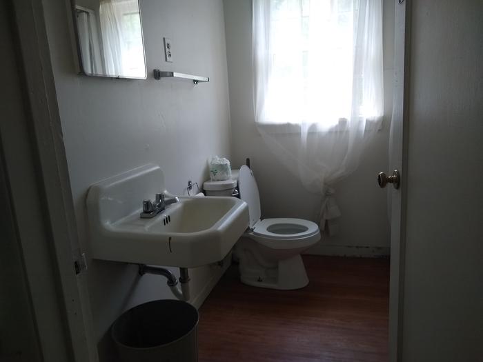 A bathroom with a toilet, sink, and trash bin.Beaver Creek Cabin indoor bathroom (running water only available in summer season).