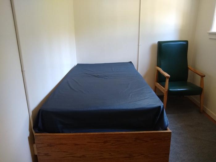 A twin sized bed next to a chair.One of two bedrooms, each with a twin-sized bed.