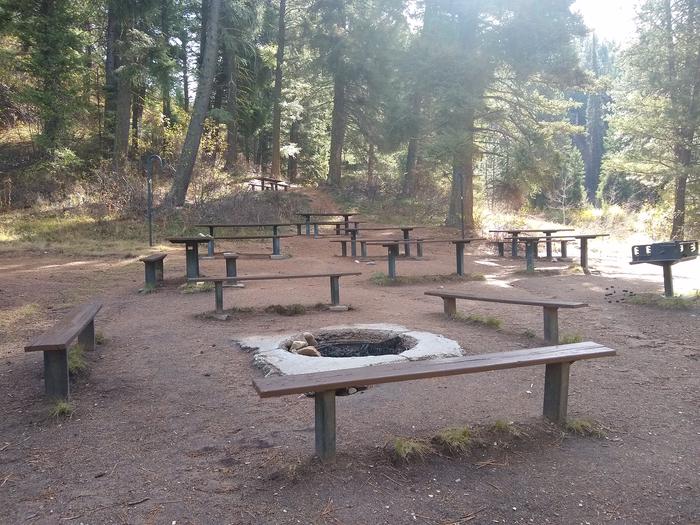 An in-ground fire pit and a raised grill, surrounded by picnic tables.Another look at main group campfire, grill, and dining area.