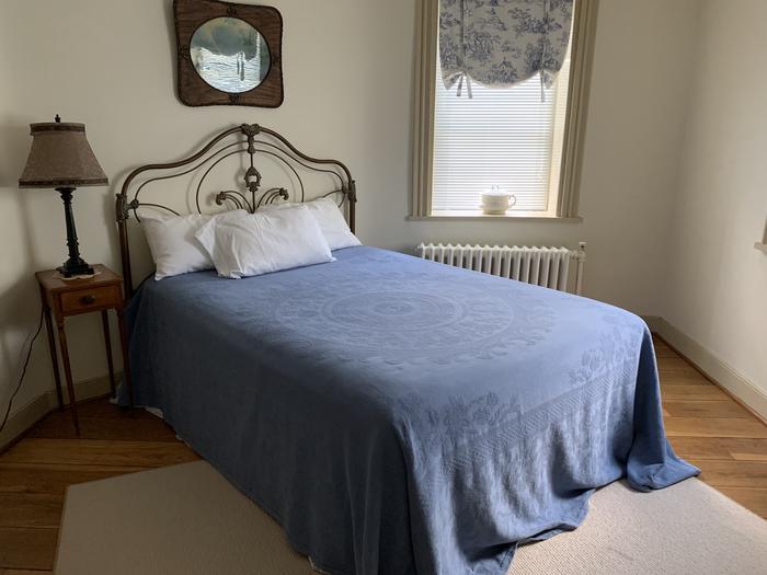 Iron framed bed with blue bedspread, side table with lampFirst Floor Bedroom