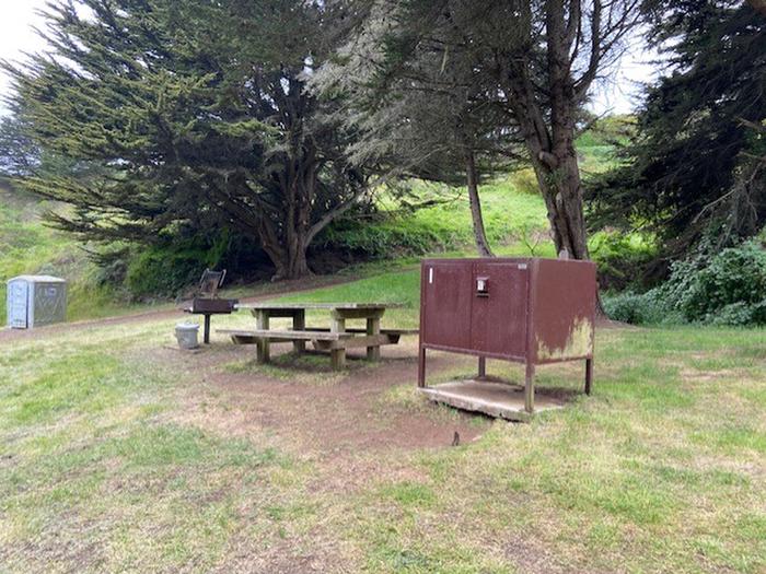 Food locker and picnic table with port-a-john in the distance Site 1