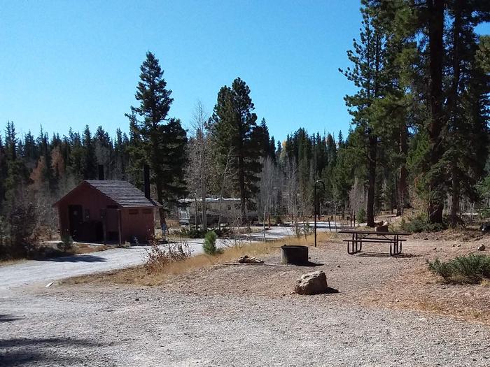Site 13 with table and gravel walkway near restroom facility and someone's camper. Campsite 13 near the restroom.