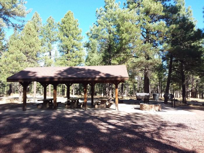 Loop G Group Campsite KG1 partially shaded with multiple picnic tables and grills, a fire pit and a pavilion