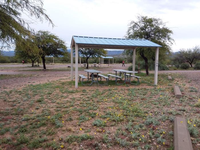 Campsite 166 with two picnic tables under a metal ramada