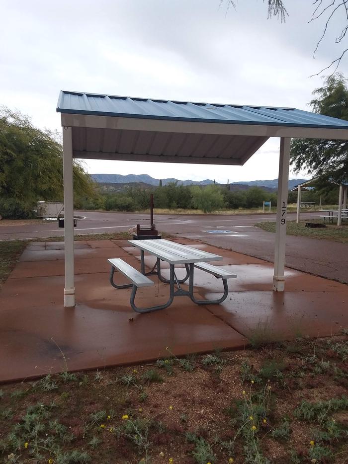 Campsite 179 with a picnic table covered by a metal ramana all on a paved patio