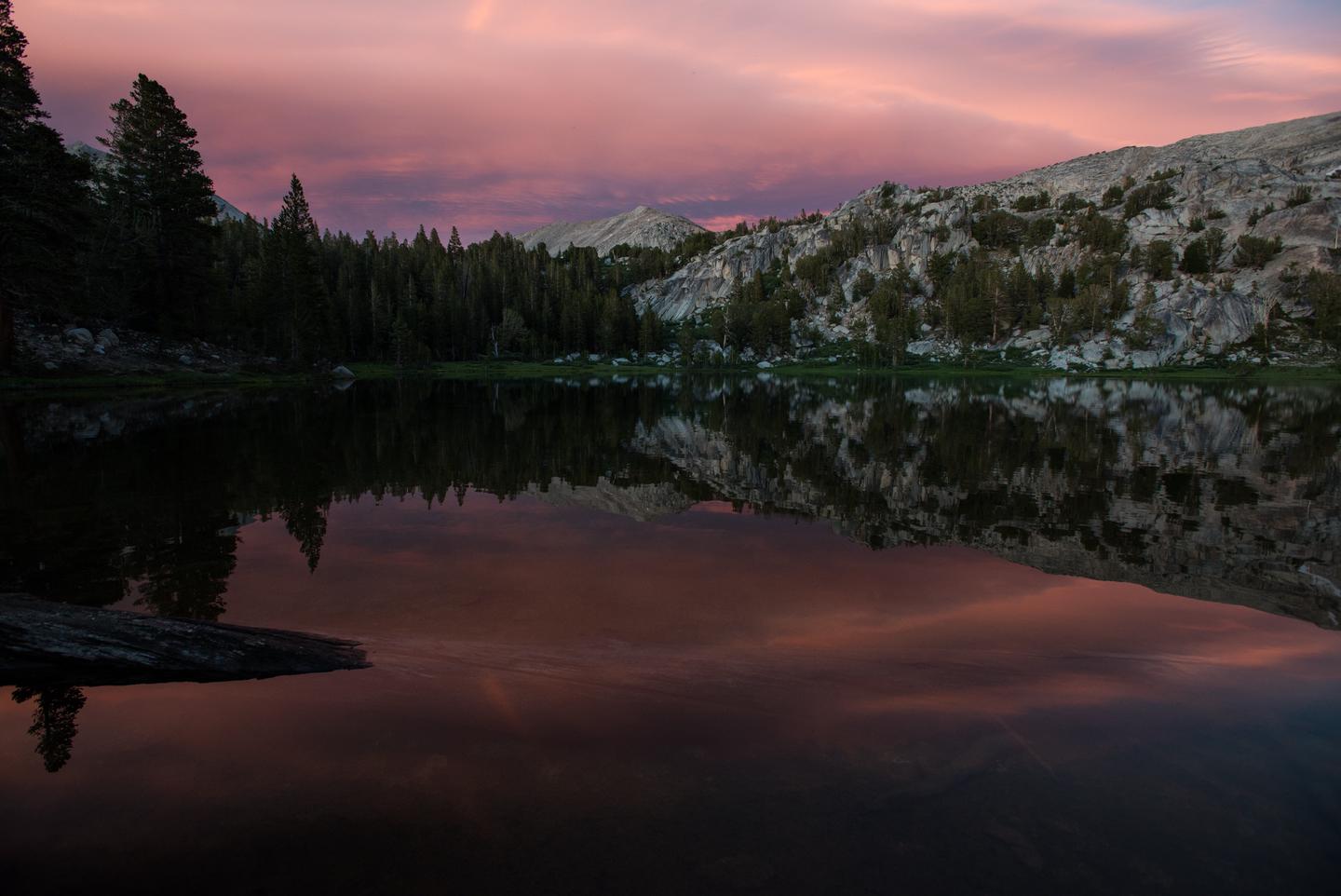 View of lake at sunset with clouds in the distanceThe last light of the day brings vibrant colors after a clearing storm. A calm High Sierra lake provides a perfect mirror for the fading light. 