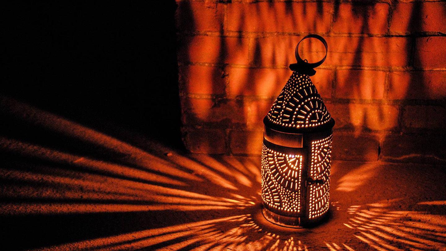 Illuminated lantern rests on floor as light and shadows are cast on the brick wall.An illuminated lantern sits on the fort floor. The metal lantern has many details which cast lace like imagery of light on the brick walls and granite floor.