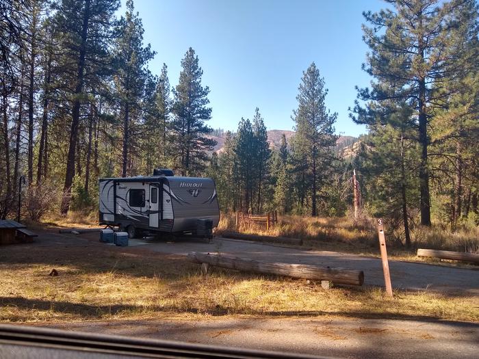 A partly sunny campsite in the woods, with a long driveway.Grayback Gulch Site 3 (trailer not included).