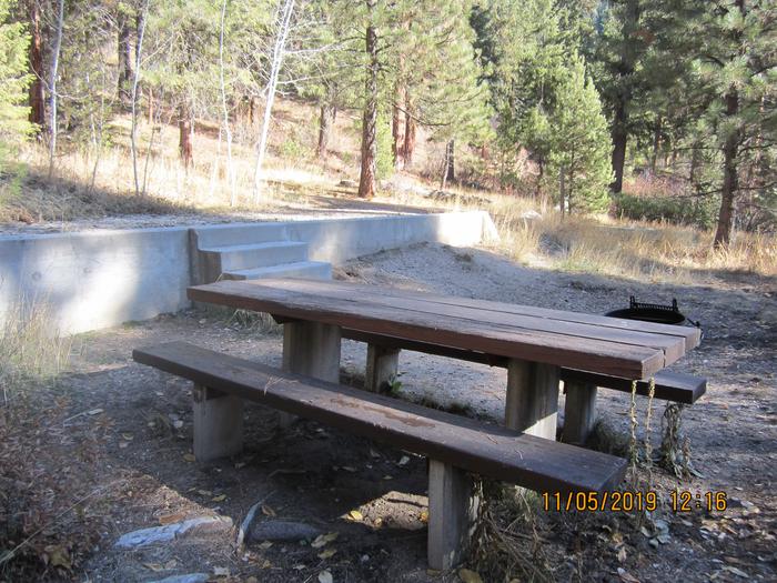 A picnic table, fire ring, and small set of stairs in a campsite.Ten Mile Site 13 has a small set of 3 concrete steps.
