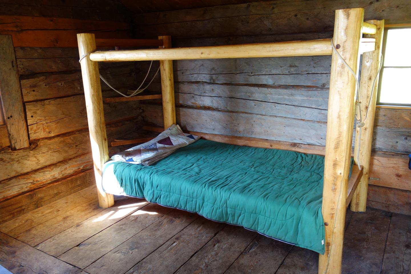 A simple wooden bed frame with blankets in a wood cabin.Two sleeping platforms in Fure's Cabin.